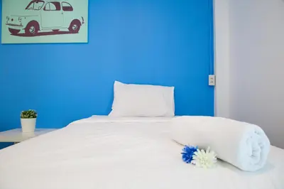 a white bed with a blue wall and a white pillow and a car at Varinda Hostel in Bangkok