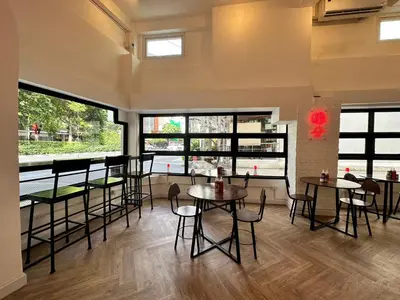 a restaurant with tables and chairs in a room with windows at The White Den Sukhumvit 44 in Bangkok