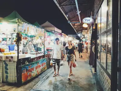 a man and a woman walking through a market at night at Double Studio, Private Bath, Shared Kitchen with Local Family by Pillows & Purrs in Bangkok