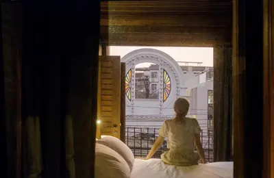 a woman sitting on a bed looking out a window at Na Tanao 1969 in Bangkok