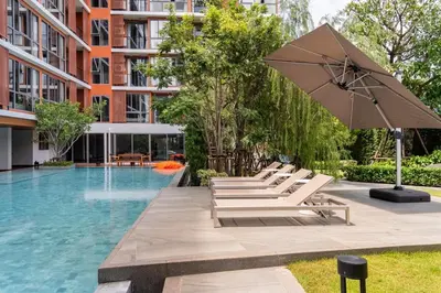 a pool with lounge chairs and an umbrella next to a building at Tierra Residences in Bangkok