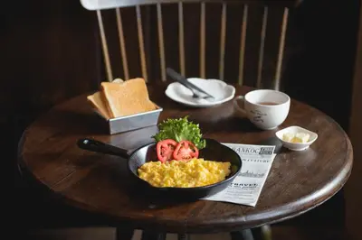 a bowl of scrambled eggs with tomatoes on a wooden table at Niras Bankoc Hostel in Bangkok