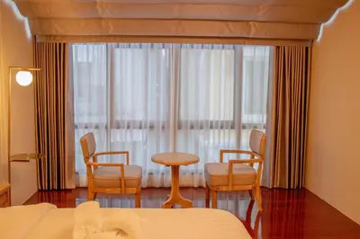 a bedroom with a bed and chairs and a window at Siri Grand Bangkok Hotel in Bangkok
