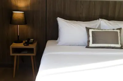 a bed with white sheets and a nightstand with a lamp at Jazzotel Bangkok in Bangkok