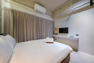 a bedroom with a large white bed and a tv at Siam Shelter Bangkok in Bangkok