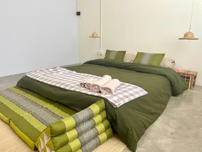 a large green bed with towels on top of it at Baan KhaoSoi - Private room in a rooftop hostel 2nd floor in Khlong San