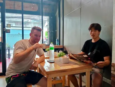 two men sitting at a table in a room at Guesthouse Bangkok BM B&B in Bangkok