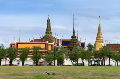 a building with three towers in a park with a bird at Mitr Inn Mrt Samyot Station - The Grand Palace in Bangkok
