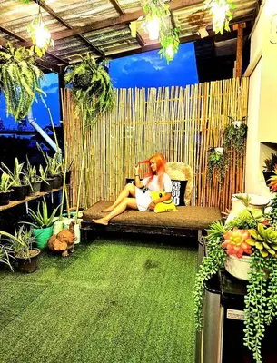a woman sitting on a couch in a room with plants at EZ Sleep @ Ratchada 19 in Bangkok