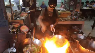 a man cooking food over a fire in a kitchen at XX Mitr Inn The Grand Palace - Mrt Samyot Station มิตร อินน์ พระบรมมหาราชวัง in Bangkok