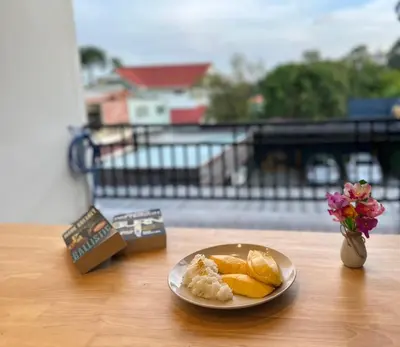 a plate of fruit on a table with a vase of flowers at Arun Heaven Bangkok in Bangkok Noi