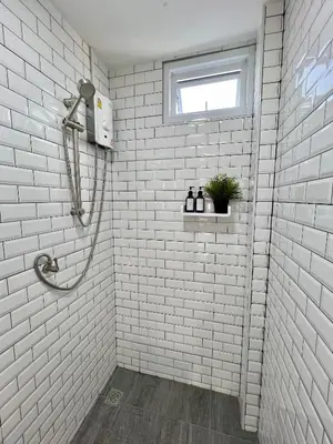 a white tiled bathroom with a shower and a window at Sabay Home in Bangkok