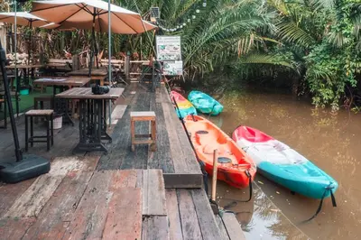 a dock with three kayaks and a table and an umbrella at Baanrongmai Canal Front Homestay in Bang Chak