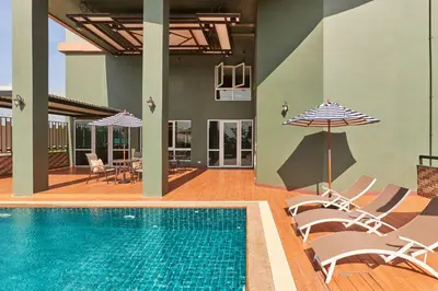 a pool with chairs and umbrellas next to a house at Cozy Donmueang Hotel in Lak Si