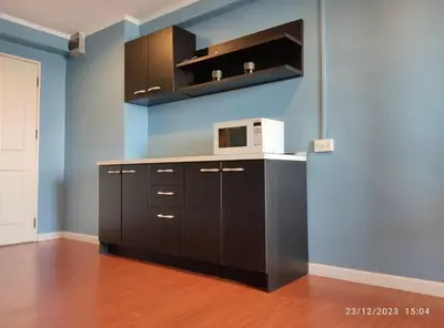 a kitchen with brown cabinets and a microwave at Regent Srinakarin18 in Amphoe Phra Khanong