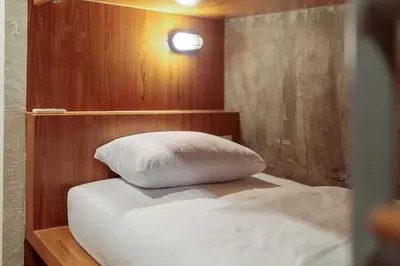 a bed with a wooden headboard and a white pillow at Rere Hostel - รีรีโฮสเทล in Bangkok