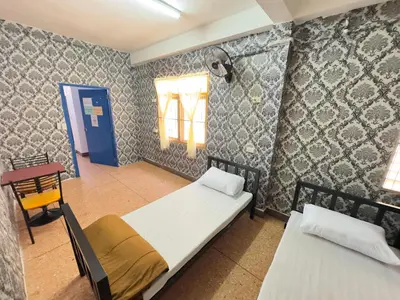 a room with two beds and a table and window at Yuma Tashi Hostel in Bangkok