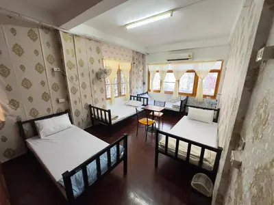 a room with three beds and a table and chairs at Yuma Tashi Hostel in Bangkok