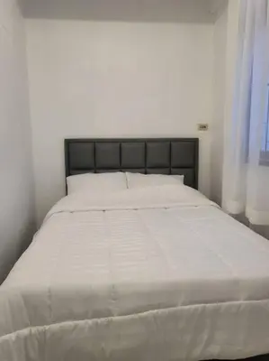 a bed in a white bedroom with a black headboard at Aunty Thong's House in Bangkok