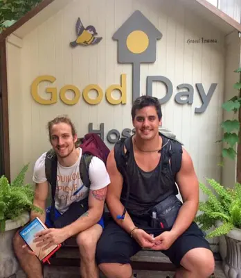 two men sitting on a bench in front of a good day sign at Good Day Hostel in Bangkok