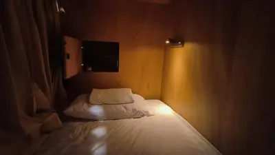 a small bedroom with a bed with white sheets and a television at BOB Hostel सुख सदन ひだまり庵 파란달여관 in Bangkok