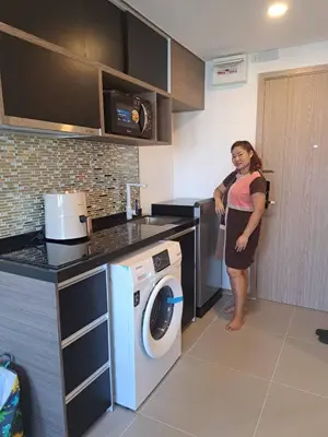 a woman standing in a kitchen with a washing machine at Cybiq Ratchada 32 by Pikul in Bangkok