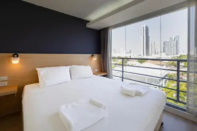 a bedroom with a white bed with a large window at GP House Express Sukhumvit 81 in Bangkok