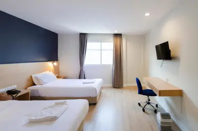 a hotel room with two beds and a desk at GP House Express Sukhumvit 81 in Bangkok