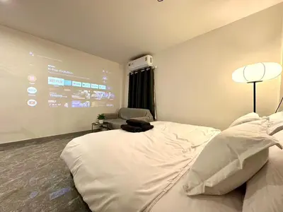 a hotel room with a large white bed and a chair at The White Den Chatuchak in Bang O