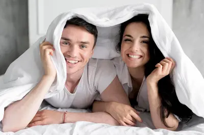 a man and woman laying in bed under a blanket at EM HOME Sukhumvit Bangkok - near Terminal 21, EM District Malls, BTS and MRT Lines in Bangkok