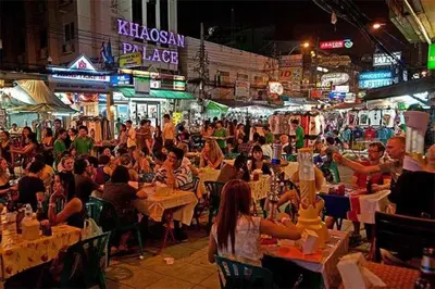 a crowd of people sitting at tables in a market at night at XX GO INN Khaosan BKK The Grand Palace - โกอินน์ ถนนข้าวสาร in Bang Bua Thong Railway Station