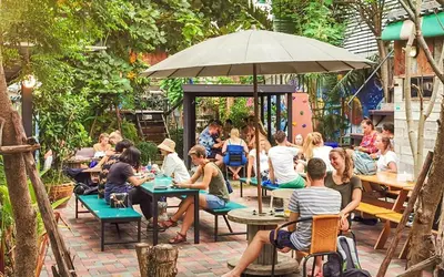 a group of people sitting at tables in a garden at Here Hostel Bangkok in Bangkok