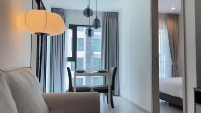 a living room with a table and a bedroom at Luxurious Downtown Apartment With Train Access Bts in Bangkok