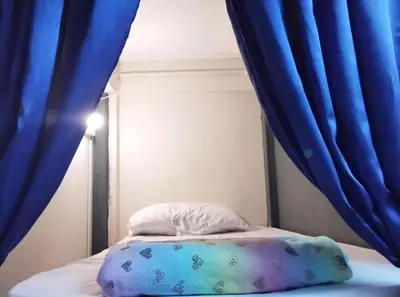 a bed with blue curtains and a white pillow at Hostel 24 Backpackers in Bangkok