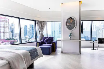 a hotel room with a bed and a chair and windows at Queensland Hotel Bangkok in Bangkok
