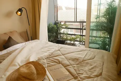 a hat and a book on a bed with a window at Enjoyo Getaway in Bangkok