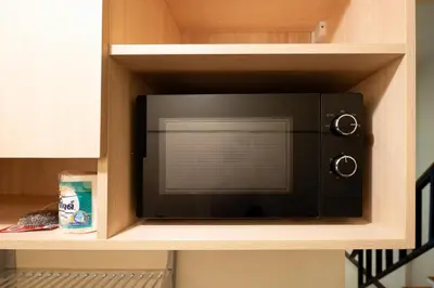 a black microwave in a wooden kitchen cabinet at OH Homes - Samsen 10 in Bangkok