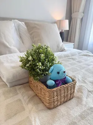 a basket with a teddy bear and a plant on a bed at New 1-Bedroom Condo for Rent 0 Meters from BTS Wutthakat in Bang Khun Thian