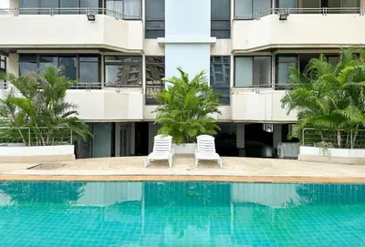 two white chairs next to a swimming pool in front of a building at Cozy, Spacious 2-Bedder with City, Park View, Near Nana BTS in Bangkok