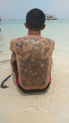 a man with a tattoo on his back sitting on the beach at Hostel in Bang Mote