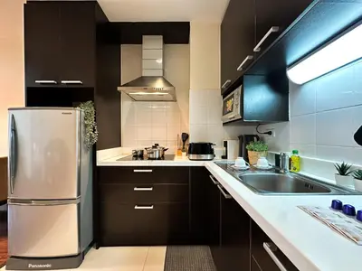 a kitchen with black cabinets and a stainless steel refrigerator at Vibrant Modern 57 SQM - Ultra Fast WiFi - BTS Thonglor in Bangkok