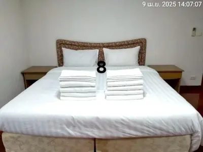a white bed with white pillows and a black clock on it at Baan Arthit in Bangkok