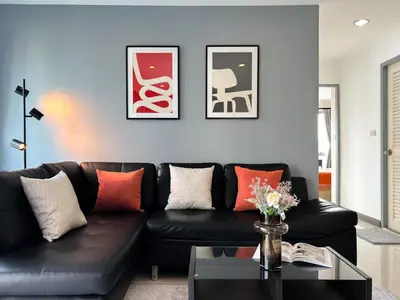 a living room with a black leather couch and framed pictures at Stylish 2BR City View - BTS St.Louis - Ultra Fast Wifi in Bangkok