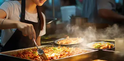 a woman is cooking food in a kitchen at I LOVE BANGKOK - Thai Style Room near Skytrain Asok, T21, and EM District Malls in Bangkok