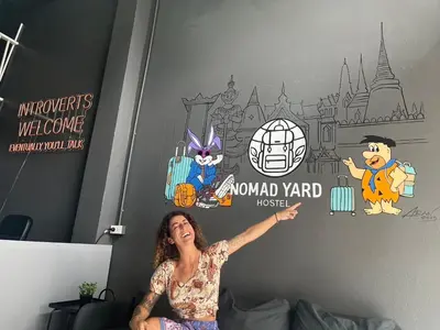 a woman sitting on a bed in a bedroom with a mural at Nomad Yard Hostel in Bangkok