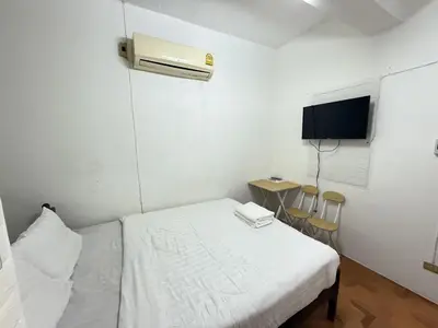 a bedroom with a bed and a tv and chairs at Happyland Guesthouse in Bangkok