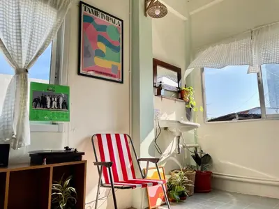 a room with a red and white chair and windows at Baan KhaoSoi - Rooftop House in Talad Noi in Samphanthawong