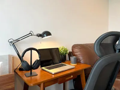 a laptop on a desk with a lamp and headphones at Cozy Park-view 1BR - Ultra Fast Wifi - BTS Bangna in Bangkok