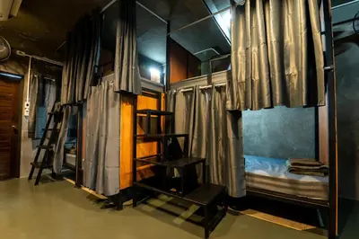 a room with bunk beds and a bunk bed with curtains at Another High Away Hostel - Bangkok in Nonthaburi