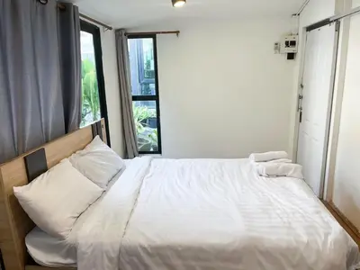 a bedroom with a bed with white sheets and a window at Chubbi 5 Room1 in Ban Bang Bamru